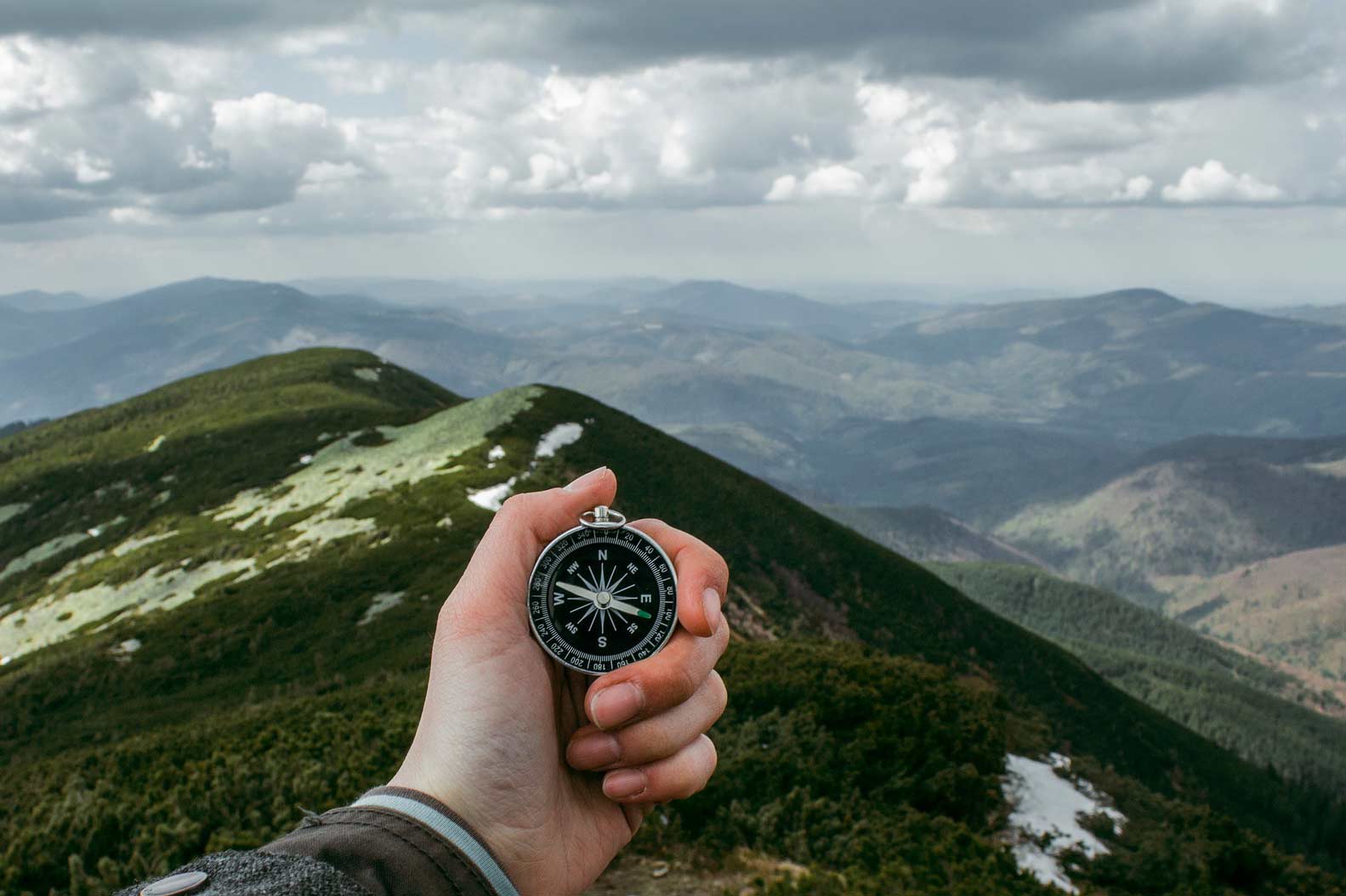 Hand holding a compass over a mountainous landscape.