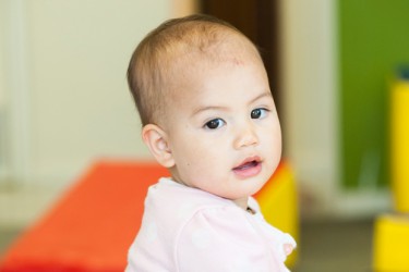 Infant standing up against a table.