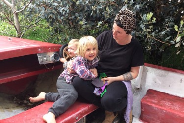 A parent with two children playing on a car at playcentre.