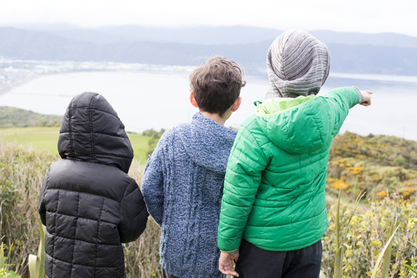 Three tamariki overlooking a bay and pointing.