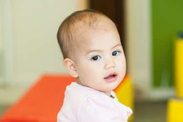 Infant standing up against a table.