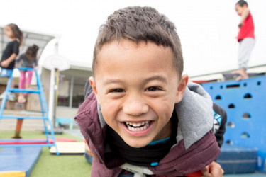 Young child leaning towards camera with a big smile