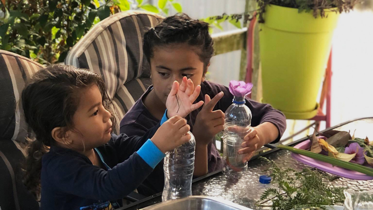 Two children using objects from outside and putting into bottles.