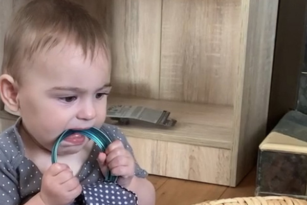 A child sucks on a metal ring with a scarf tied to it from a treasure basket.