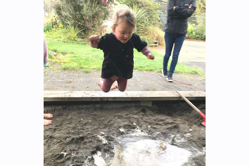 Eliza mid jump into a muddy puddle in the sandpit to explore saturation.