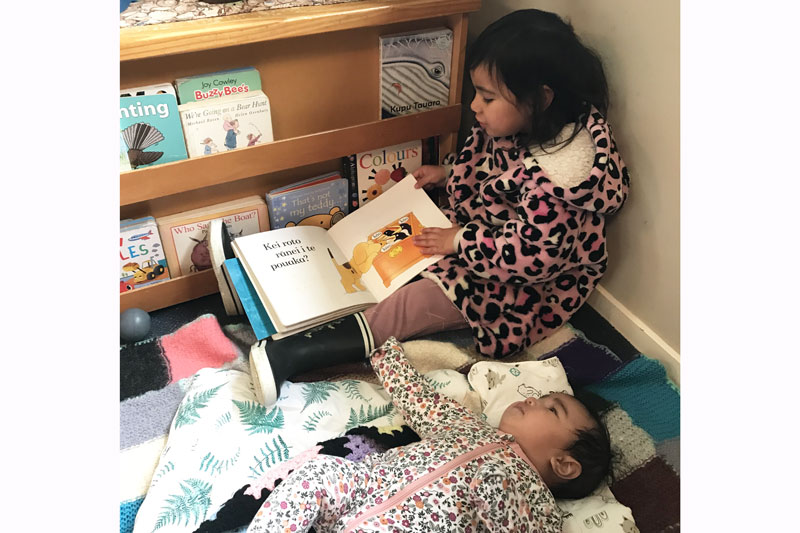 Te Ataraupo being a tuakana by reading a story to a baby.