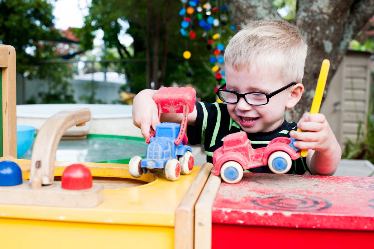 A child happily playing with some vehicles.