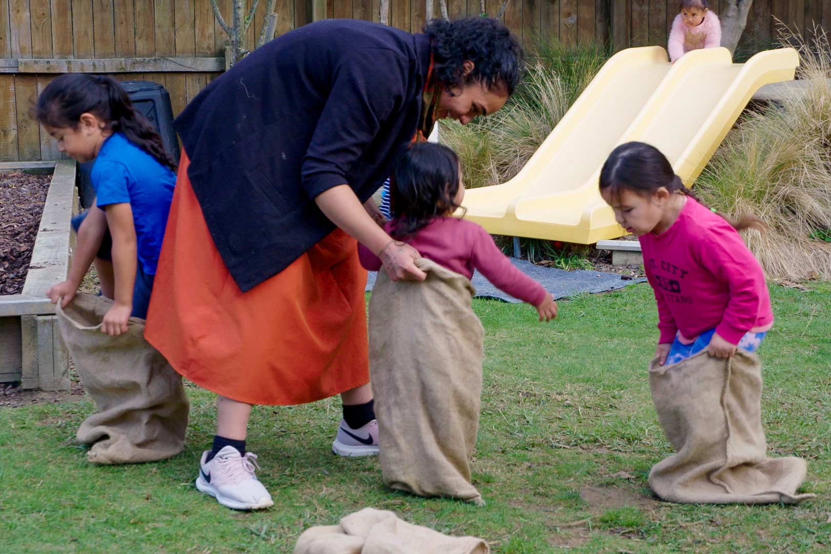 A kaiako helps a child into a sack while others are also climbing into sacks.