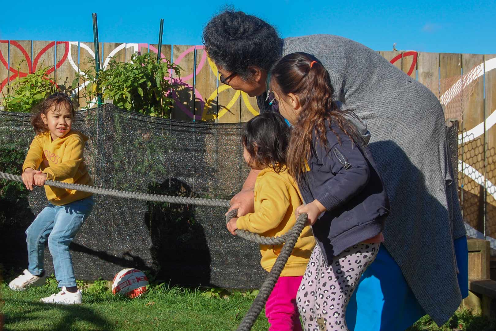 A kaiako helps tamariki with a tosogā maea, tug of war.