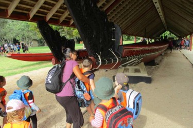 Child being lifted up to to hongi the waka Ngātokimatawhaorua.