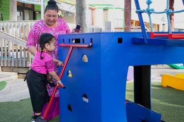 A child climbing a ladder while talking with a kaiako. 