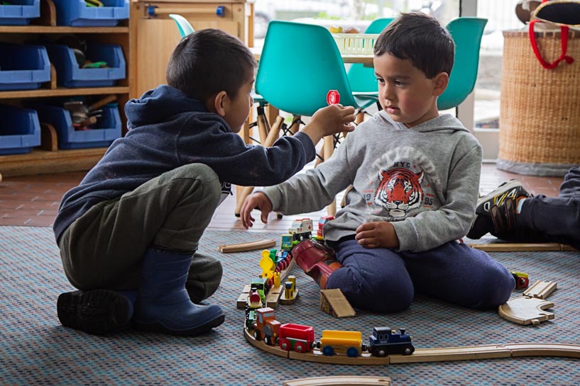 Two tamariki talking together over building a train track.