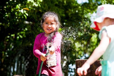 Child watering plants with a hose. 